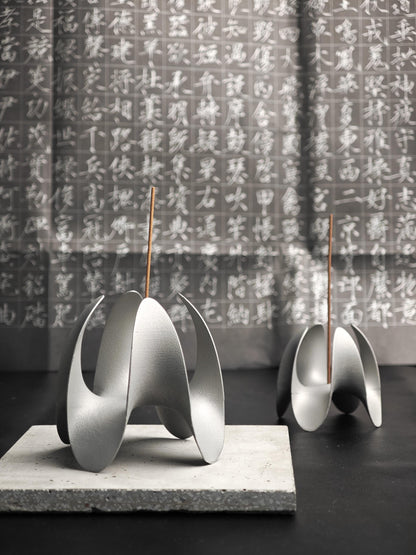 A sculptural incense holder crafted from aerospace-grade aluminum alloy, featuring a flowing cyberpunk-inspired form and a matte silver finish. Designed for modern interiors, meditation spaces, or futuristic decor setups.